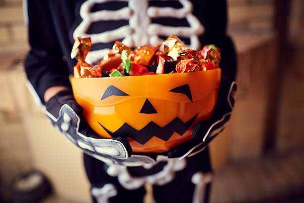 Skeleton costumed child, holding a pumpkin-shaped bowl of candy